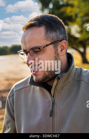 close-up profile shot of a happy, middle-aged man with a beard and glasses, laughing or smiling in a natural, sunlit outdoor setting Stock Photo