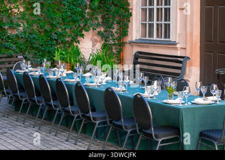 A long table is meticulously set with glassware, plates, and napkins for an outdoor banquet or reception Stock Photo
