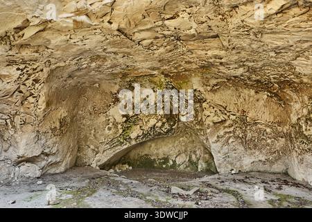 Natural cave interior with textured rock walls, visible moss and dirt floor, showcasing geological formations and shadows in a secluded environment Stock Photo