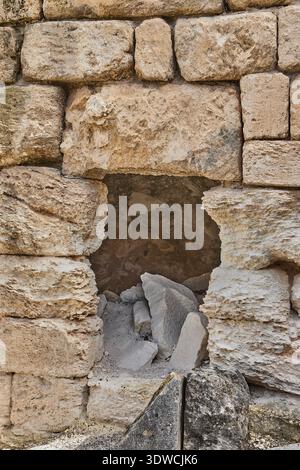Ancient stone wall with a rectangular opening revealing broken stones and debris inside, showcasing weathered textures and historical construction Stock Photo