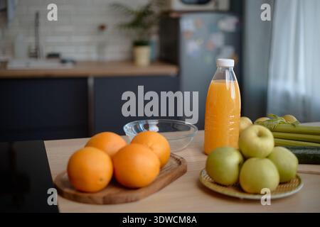 Fresh Oranges and Green Apples Arranged with Bottle of Juice on Kitchen Table Stock Photo