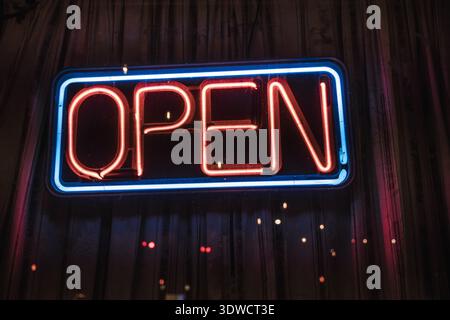Bright neon open sign glowing in red and blue colors at night on a storefront window. Stock Photo