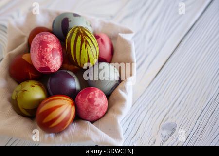 Colorful handmade Easter eggs in a basket sit on a rustic white wooden surface. The eggs display various intricate patterns and vibrant colors, includ Stock Photo