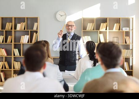 Professor leading university lecture for adult students in book lined classroom Stock Photo