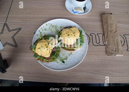 Two plates of eggs benedict are served at a cafe in Sibiu Romania during brunch. A person sits nearby with a coffee. Stock Photo
