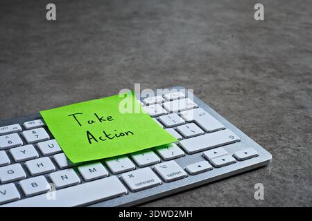 "Take Action" sticky note left on keyboard. The bright note stands out against the keys, symbolising motivation, and productivity. Stock Photo