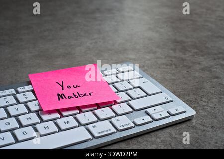 "You Matter" sticky note left on keyboard. The bright note stands out against the keys, symbolising motivation, and productivity. Stock Photo