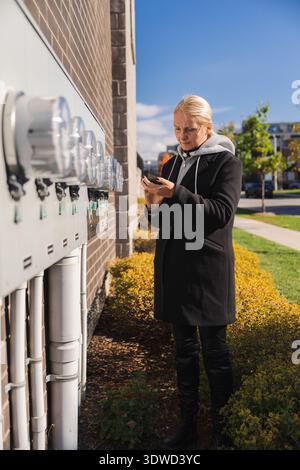 Woman checking outdoor electricity meters on building wall using smartphone Stock Photo