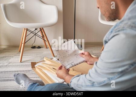 Man assembling furniture, reviewing instructions while sitting on the floor Stock Photo