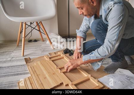 Man kneeling, assembling flat pack furniture using instructions on the floor Stock Photo
