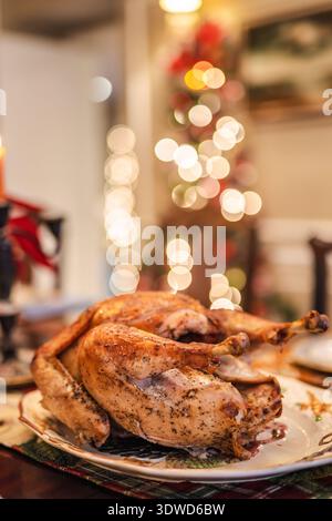 Roasted holiday turkey served on a festive table with warm Christmas lights glowing in the background. Stock Photo
