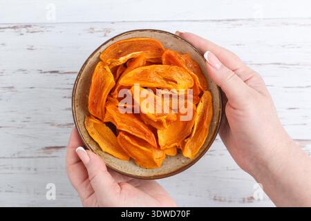 A woman holds a plate with slices of ripe dried persimmon in a plate on the table. A healthy snack. A treat. Selective focus, top view Stock Photo