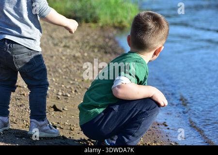 Close up side portrait of toddler boy looking thoughtfully at river water. Outdoor childhood moment captured in natural sunlight with soft blurred bac Stock Photo