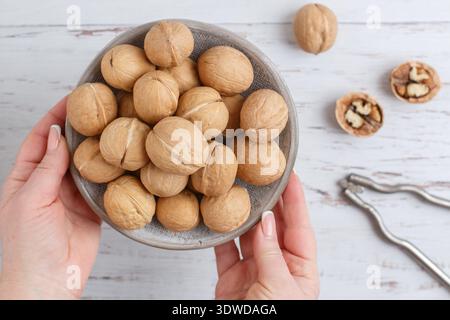 Walnuts and chopping irons on the table. A woman holds a plate of nuts in her hands. Selective focus, top view Stock Photo