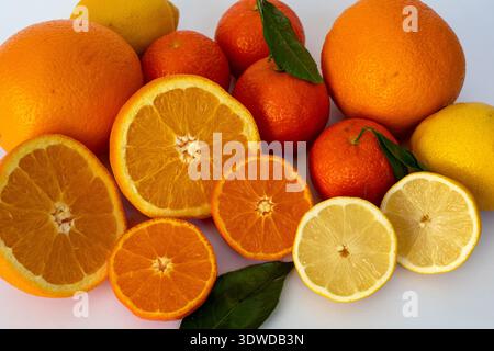 A vibrant close-up of various citrus fruits including whole and halved oranges, lemons, and tangerines with green leaves. The bright composition on a Stock Photo