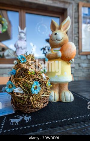 Ceramic bunny with orange egg beside twig nest in rustic cafe scene Stock Photo