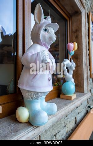 Easter bunny statue in raincoat on stone windowsill with egg Stock Photo