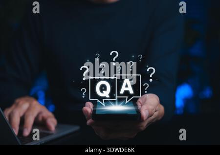Q&A Chat Interface and Online Support Concept. Person holds smartphone with speech bubbles marked Q and A surrounded by question marks, Stock Photo