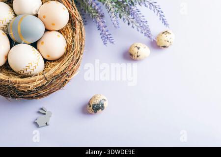Easter eggs in rustic nest with quail eggs and lavender on pastel background. Easter holiday greeting card. Top view, copy space. Stock Photo