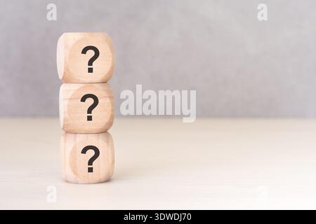 Business concept of uncertainty, confusion, and support. A vertical stack of three wooden blocks with question marks on a neutral background with copy Stock Photo