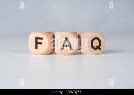Three natural wood cubes arranged in a row on a pale tabletop, each printed with a single letter forming FAQ. The clean, minimal composition conveys f Stock Photo