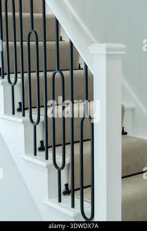 Interior of a London house featuring a classic staircase with elegant black metal railing and neutral toned carpet. The design blends contemporary and Stock Photo