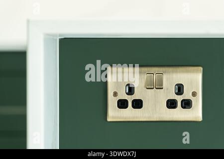 A close up view of a brass wall socket on a dark green wall in a stylish London home. The modern design enhances the contemporary interior aesthetic. Stock Photo