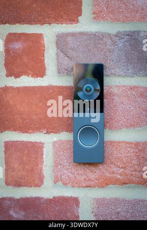 A sleek, modern doorbell is mounted on the vibrant red brick exterior of a house in London, United Kingdom, providing both security and style to the h Stock Photo