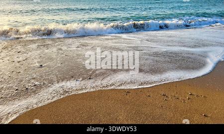 Close-up view of foaming waves rolling onto the sandy beach in the soft morning light along the Costa Brava in Spain Stock Photo