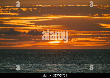 A breathtaking sunset over the tranquil ocean in Galicia, Spain, casting vibrant orange and golden hues across the sky and reflecting beautifully on t Stock Photo