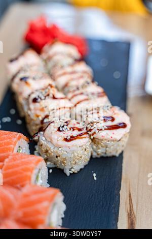 Assorted sushi rolls, featuring salmon and various toppings, artfully arranged on a black slate platter. The vibrant presentation highlights the fresh Stock Photo
