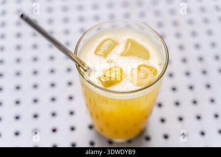 A refreshing glass of orange juice with ice cubes and a stainless steel straw, placed on a polka dot background. Perfect for a cool, thirst quenching Stock Photo