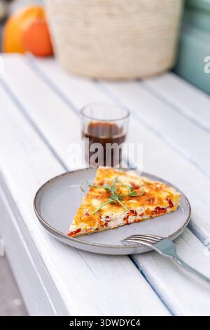 A delightful slice of quiche served on a white plate with a fork on the side, paired with a refreshing drink in a clear glass. The setting is a light- Stock Photo