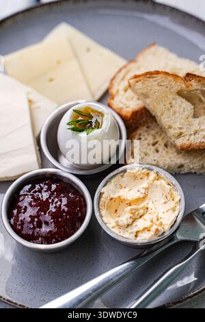 A delectable breakfast plate featuring slices of cheese, a perfectly cooked egg, creamy butter, fresh bread, and a tangy sauce. Served on a clean whit Stock Photo