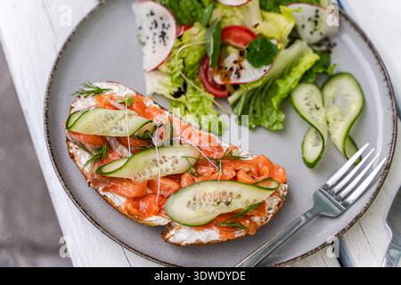 A delicious toast with salmon, fresh cucumber, and micro herbs, paired with a vibrant salad featuring leafy greens, tomatoes, radish, and a sprinkle o Stock Photo