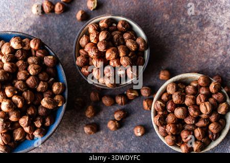 A close-up image of organic hazelnuts in three rustic bowls on a dark, textured background. The nuts are shelled and ready for cooking or snacking, em Stock Photo