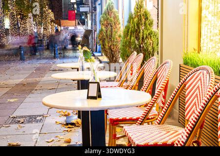 Empty outdoor café with red and white chairs lined along tables in Tbilisi, Georgia, adorned with festive Christmas lights, capturing the season's joy Stock Photo