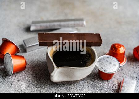 A rich espresso served in a ceramic cup accompanied by a bar of chocolate. Surrounded by shiny coffee capsules, offering a perfect blend of indulgence Stock Photo
