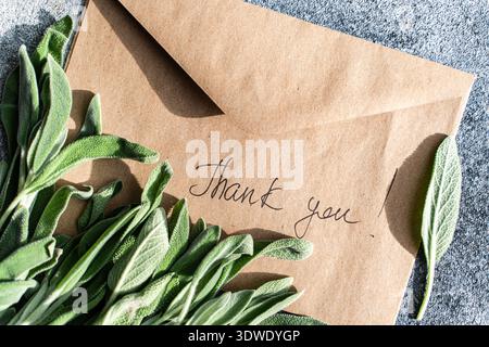 Fresh sage leaves are artfully arranged on a rustic envelope with a handwritten Thank you note. The combination of natural textures creates a warm, in Stock Photo