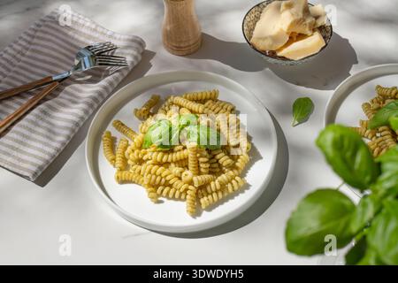 A plate of delicious penne pasta tossed in vibrant green basil pesto, garnished with fresh basil leaves. The dish is served on a white plate perfect f Stock Photo