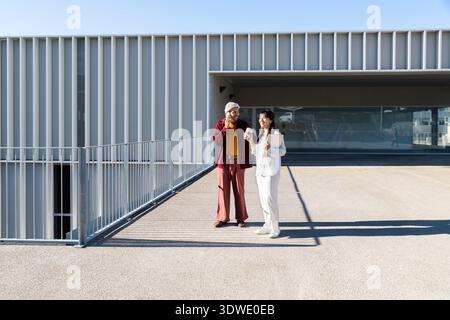 Two business professionals having a conversation outside a modern building. They appear engaged and friendly, standing on a sunny day, with the struct Stock Photo