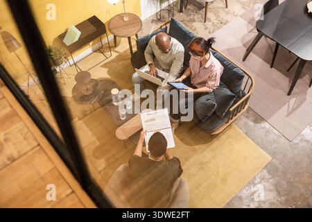 Diverse team working in a modern coworking space, using digital devices and printed documents. Engaged in a collaborative meeting, showcasing contempo Stock Photo