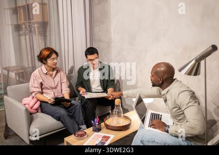 A diverse team of coworkers collaborating in a modern office environment. They are engaged in discussion, sharing ideas, and utilizing technology for Stock Photo