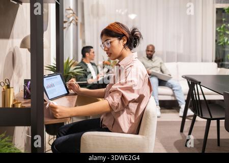 Professionals collaborating in a stylish coworking space, engaging in discussions and analyzing data on laptops and tablets. The environment fosters c Stock Photo