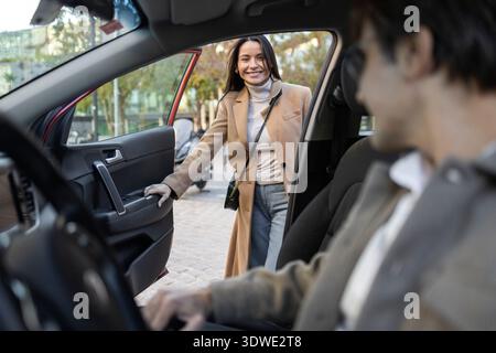 A young couple prepares for an exciting road trip adventure. The woman opens the car door with a smile, while the man waits inside, ready to embark on Stock Photo