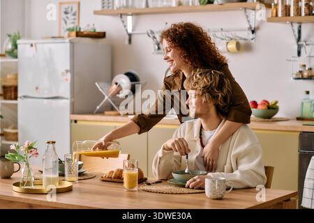 A redhead woman warmly serves orange juice to her blonde partner at a cozy breakfast table. Stock Photo