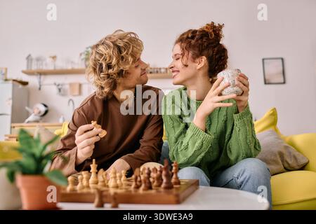 In a bright, stylish apartment, a curly-haired couple shares smiles while playing chess together. Stock Photo