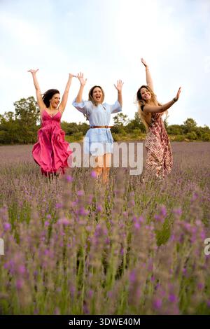 Three women are joyfully jumping in a vibrant lavender field, with lush lavender blossoms surrounding them. They are celebrating friendship in a seren Stock Photo