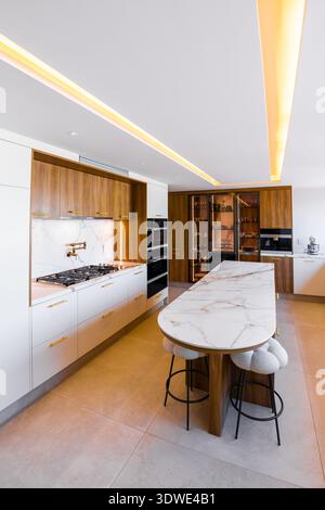 A stunning luxury kitchen featuring a sleek kitchen island with a marble countertop, complemented by warm wood cabinetry. The minimalist, contemporary Stock Photo