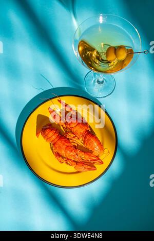 A delightful arrangement featuring boiled crayfish resting on a bright yellow plate beside an elegant martini glass with olives, set against a vivid t Stock Photo